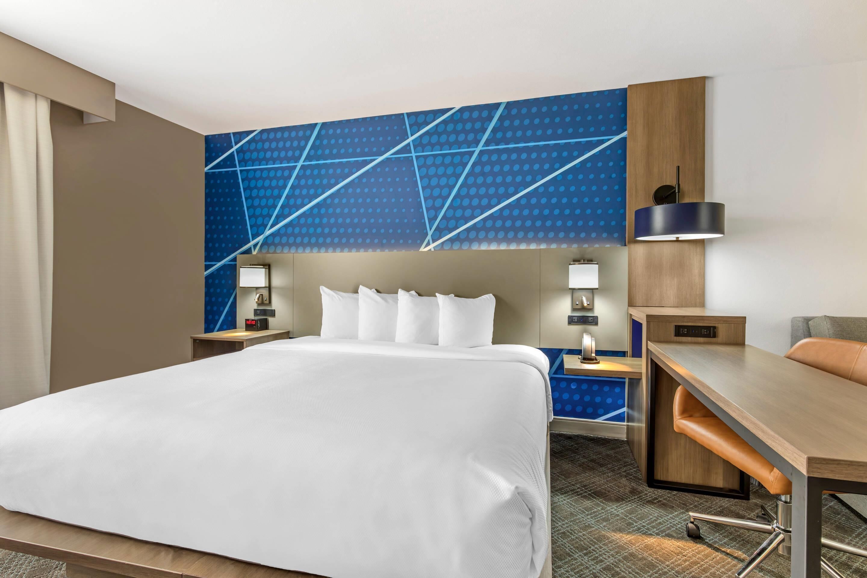 A hotel room with a large bed, a desk, and a chair. There are two bedside tables with lamps.