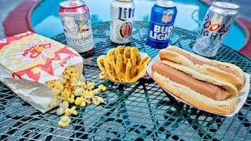 Una mesa con un hot dog, palomitas de maíz y tres latas de cerveza.