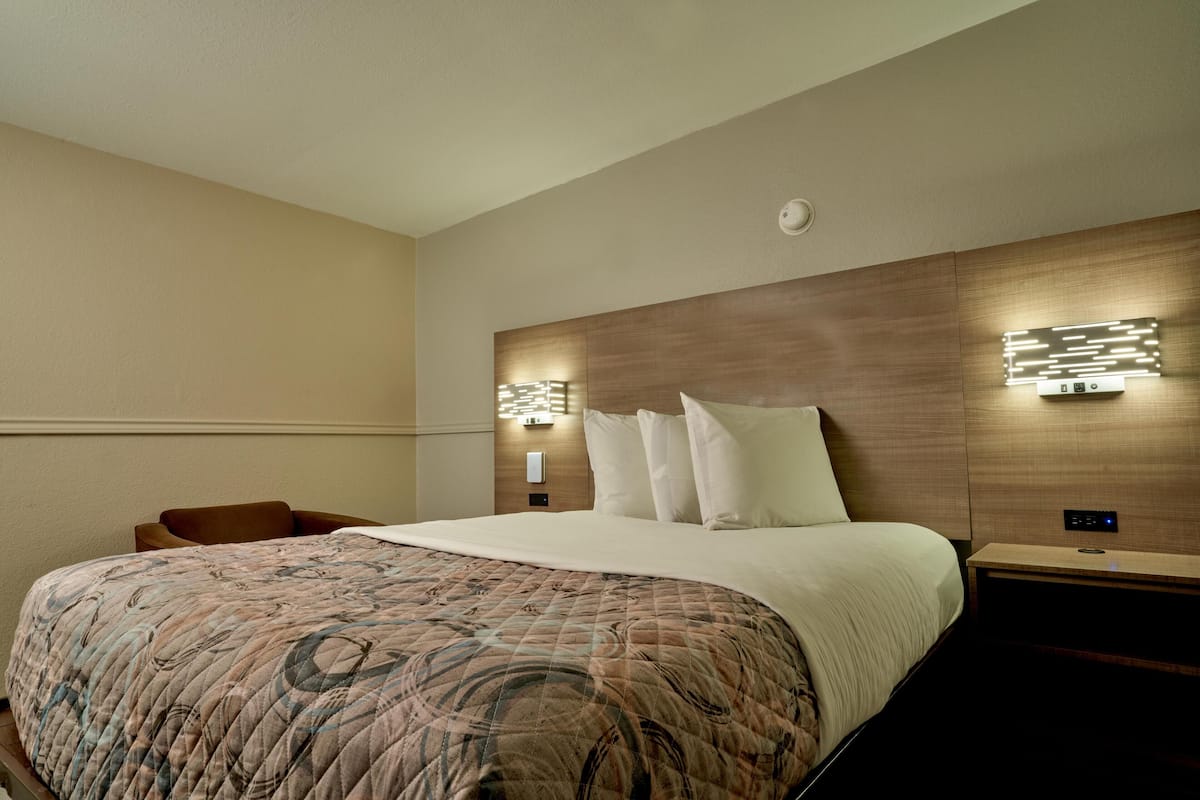 A hotel room with a large bed, two bedside tables, a chair, and wall-mounted lighting.