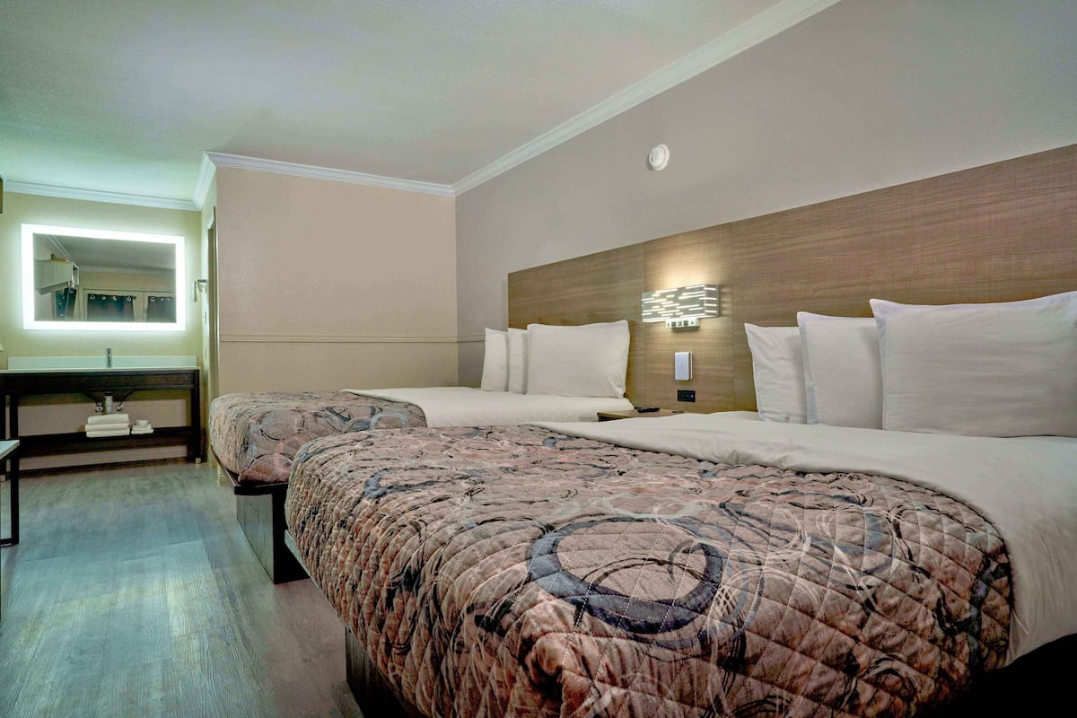 A hotel room with two beds, a bedside table, a mirror, and a wall-mounted light fixture.