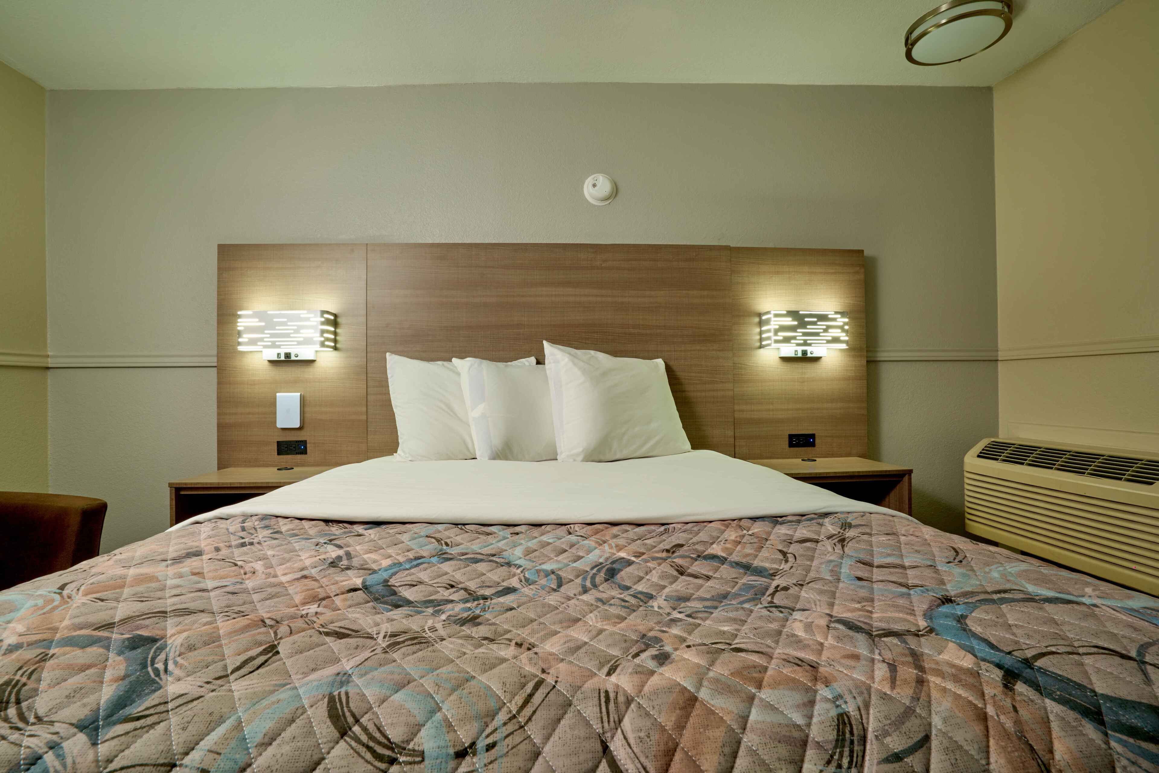 Une chambre d’hôtel avec un grand lit, deux tables de chevet, un luminaire fixé au mur et un lustre au plafond.