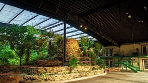 An indoor atrium with a glass ceiling, stone walls, and tropical plants. - Family Garden Inn & Suites (Laredo)