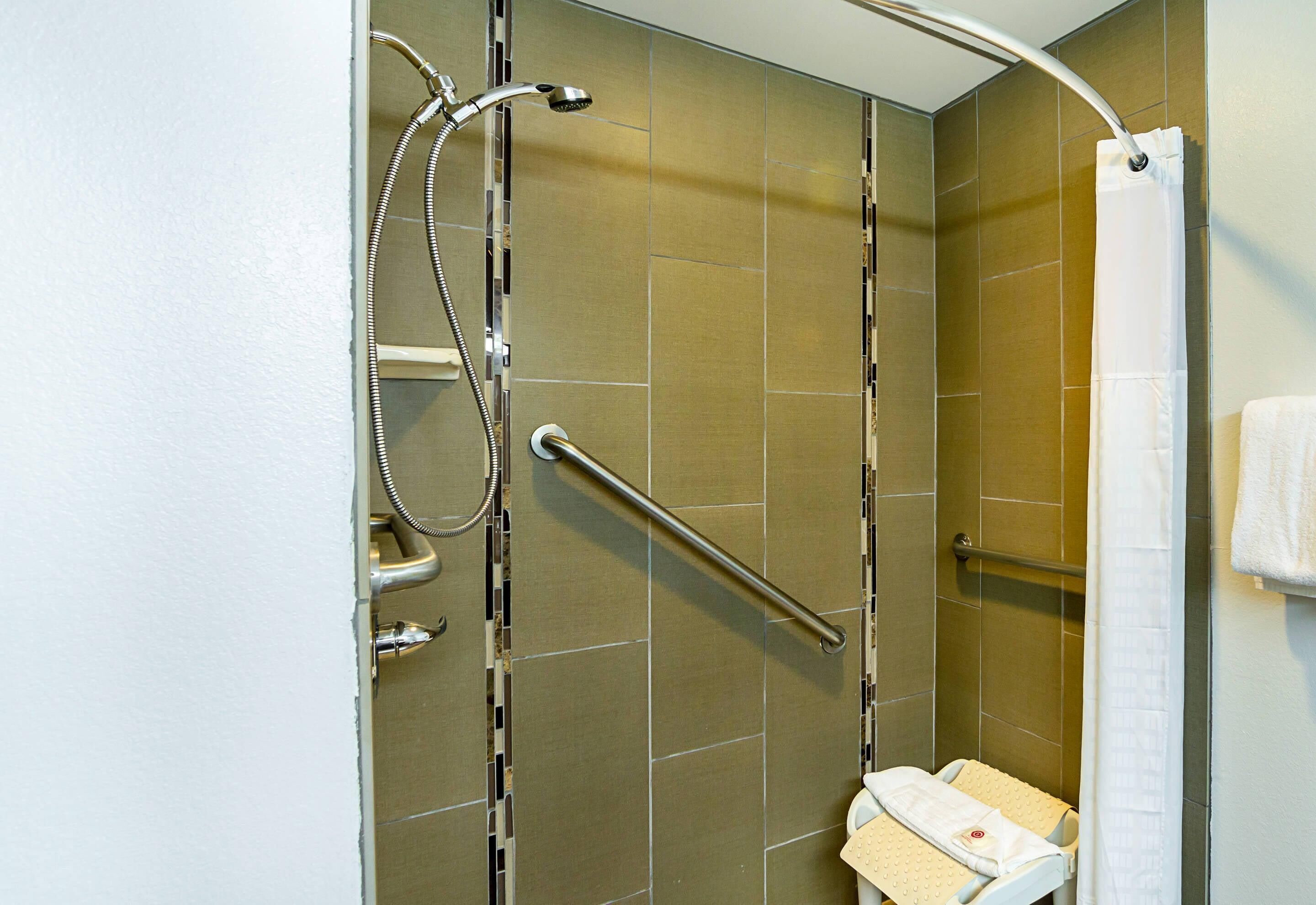 A shower area with a grab bar, a handheld showerhead, and a towel rack.