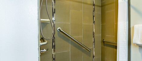 A shower area with a grab bar, a handheld showerhead, and a towel rack.