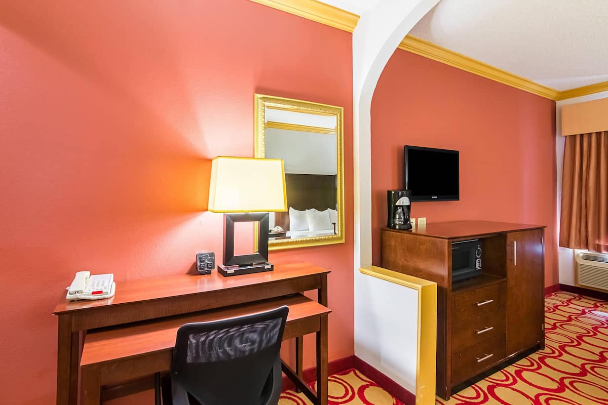 Habitación de hotel con escritorio, silla, lámpara, teléfono, espejo, televisión y armario.