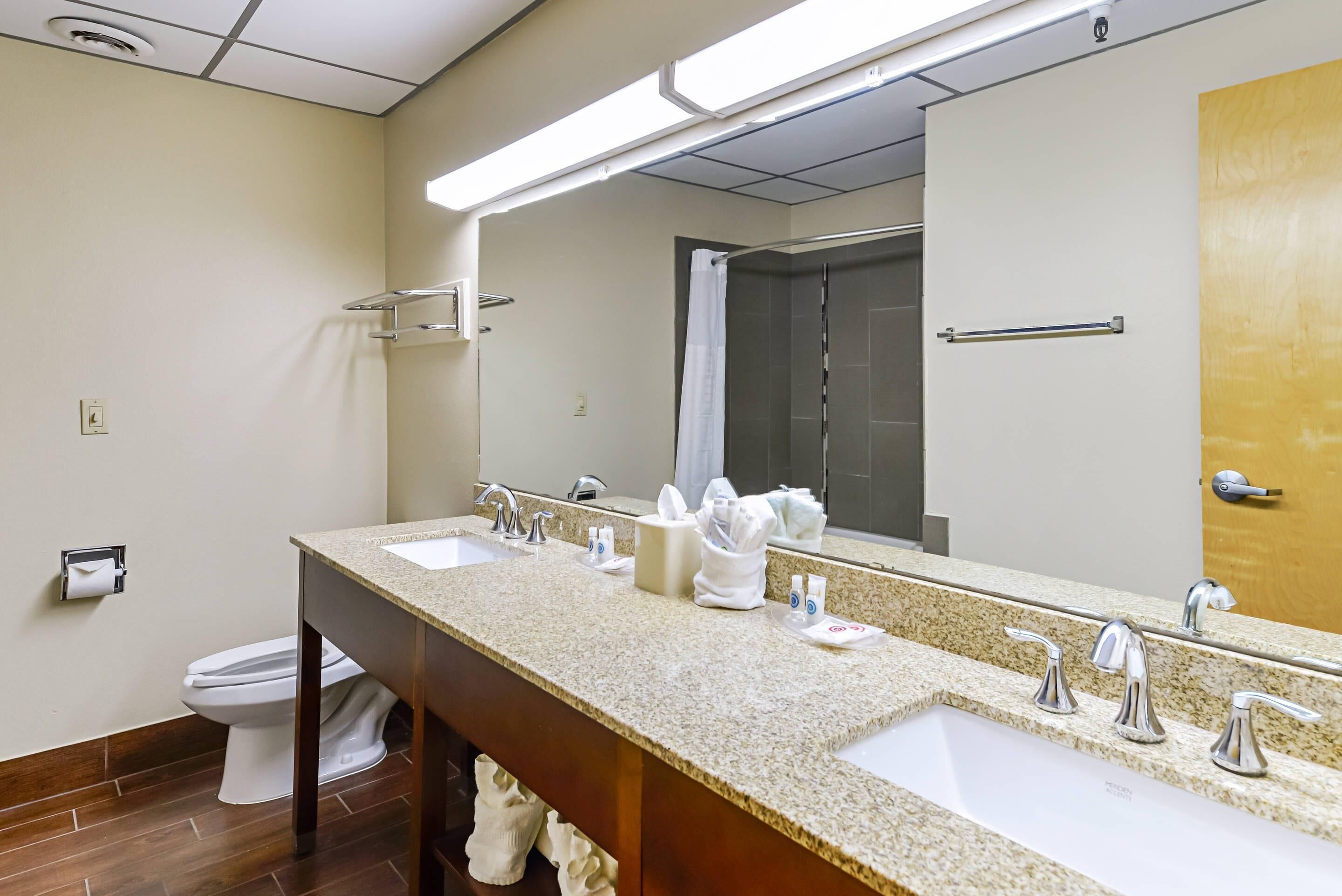 A hotel bathroom with two sinks, a mirror, and a shower.