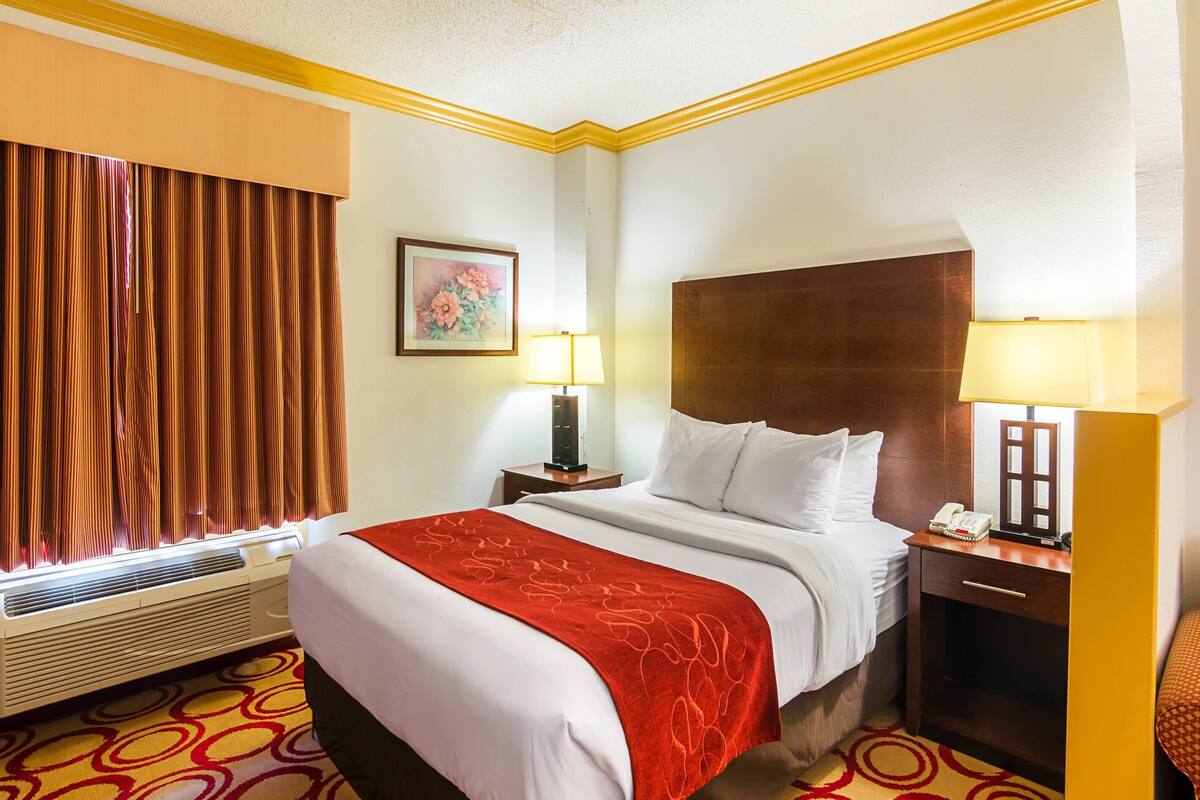 Habitación de hotel con una cama grande, dos mesitas de noche con lámparas, un calentador y una ventana con cortinas.