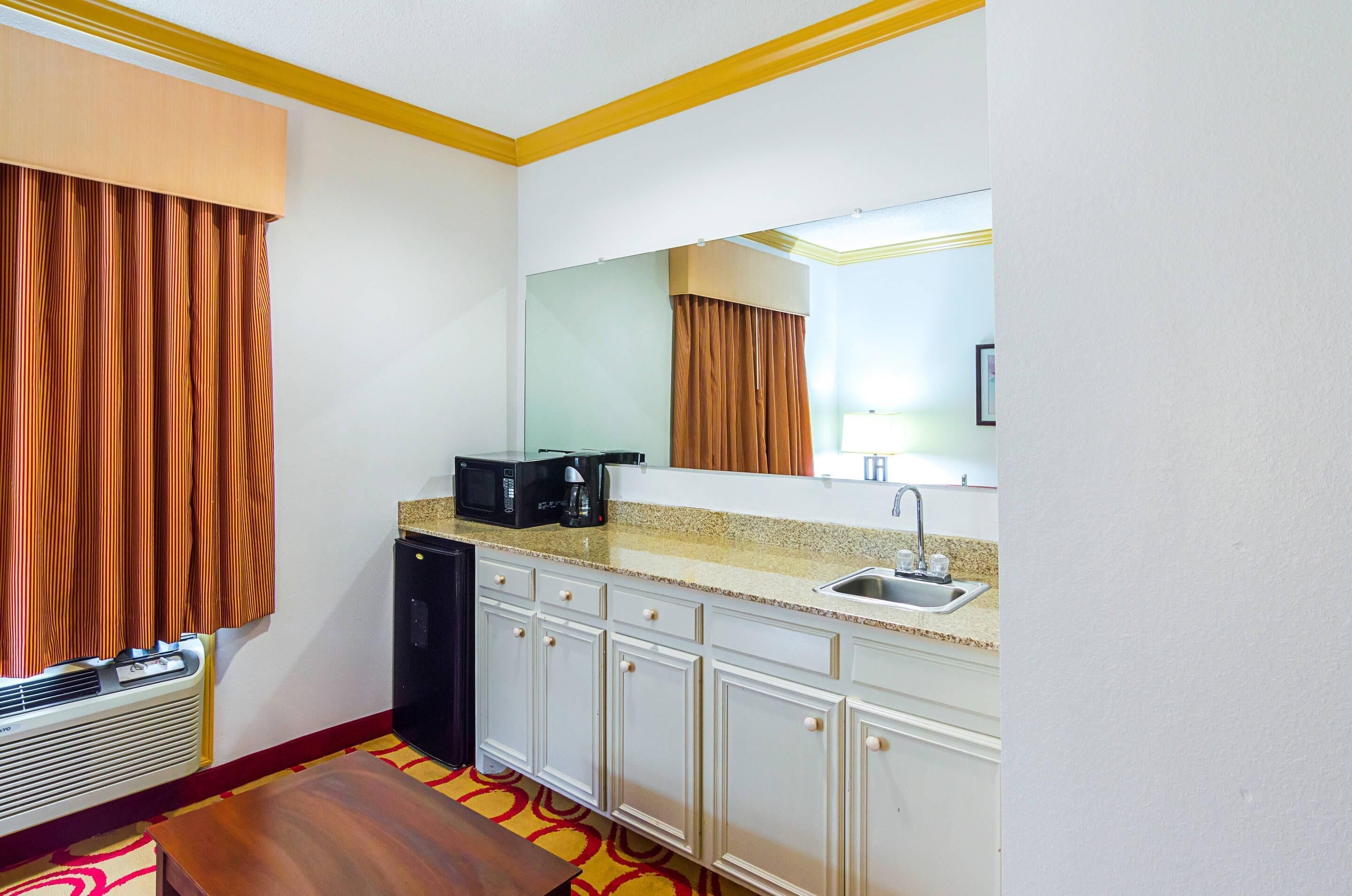 A compact hotel room with a kitchenette, a microwave, a sink, and a large mirror.