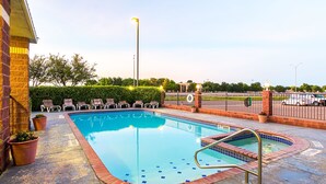 A rectangular swimming pool with a tiled edge, surrounded by a brick border and a metal handrail.