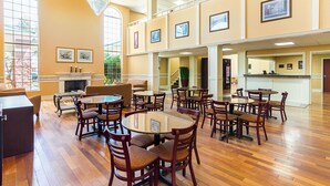 A spacious dining area with multiple round tables and chairs, a fireplace, and large windows allowing natural light.