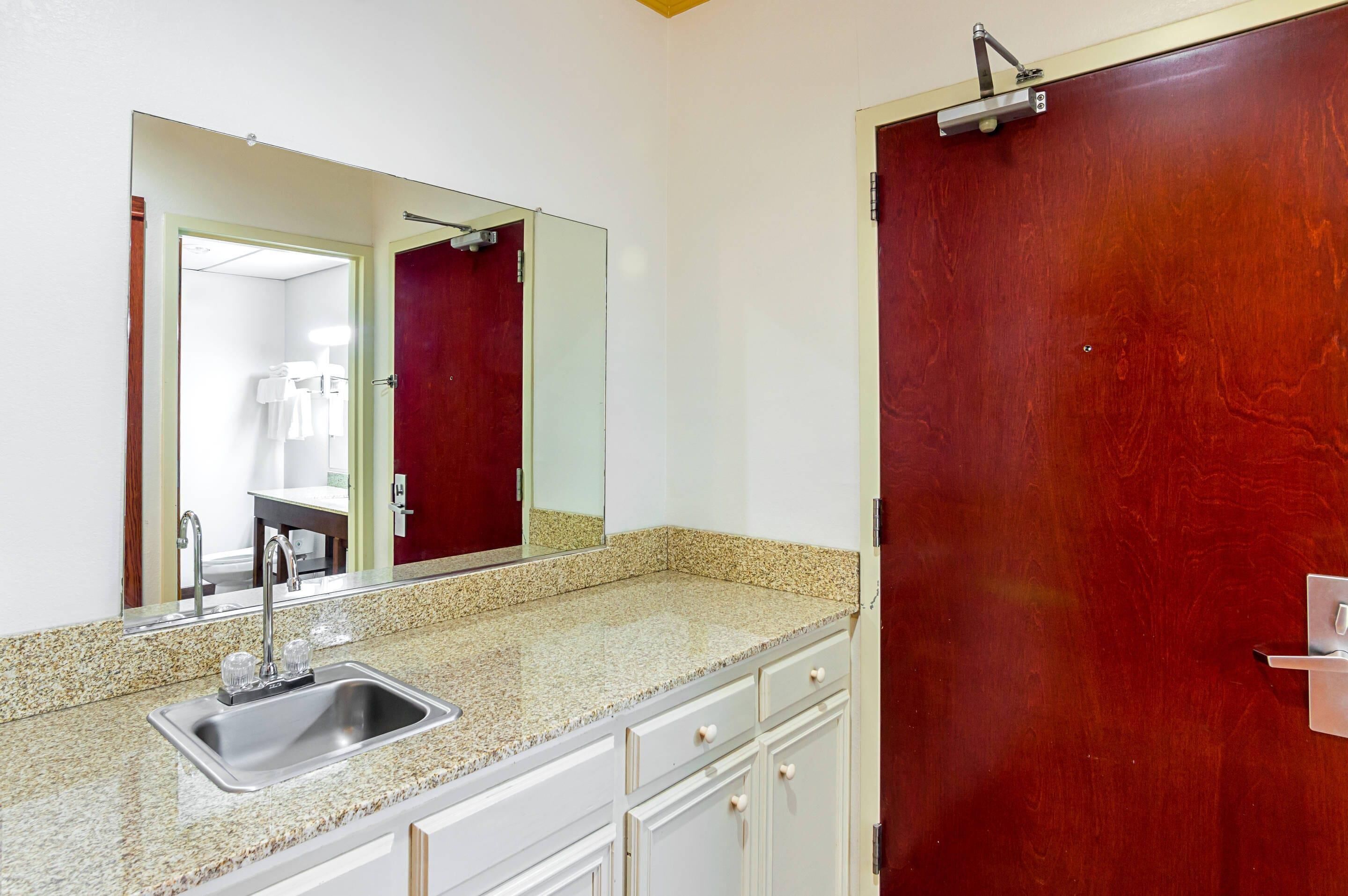 Une salle de bain avec un comptoir en granit, un lavabo, un miroir et une porte rouge.