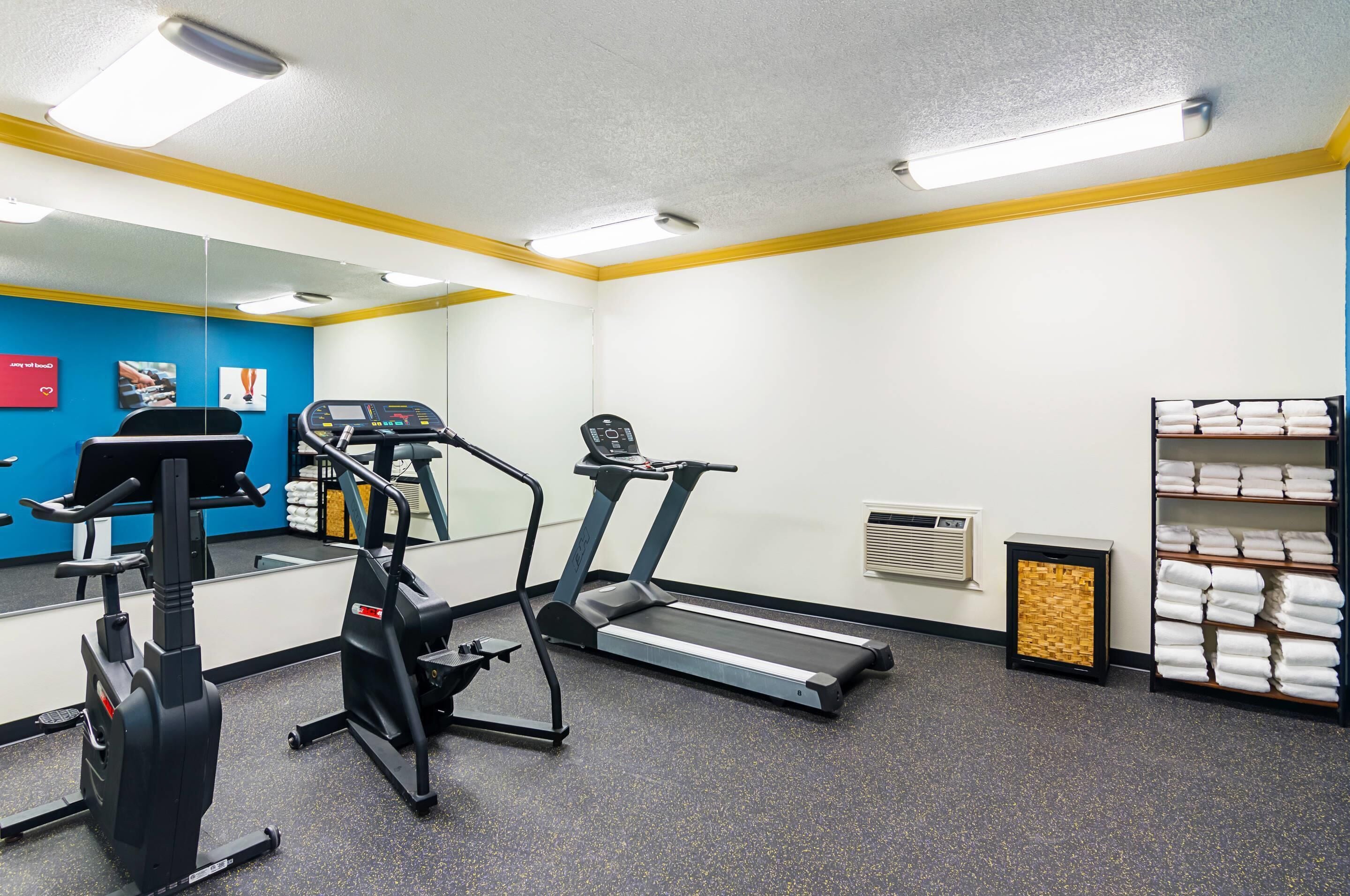 A gym with exercise equipment, a mirror, a towel rack, and a wall-mounted air vent.