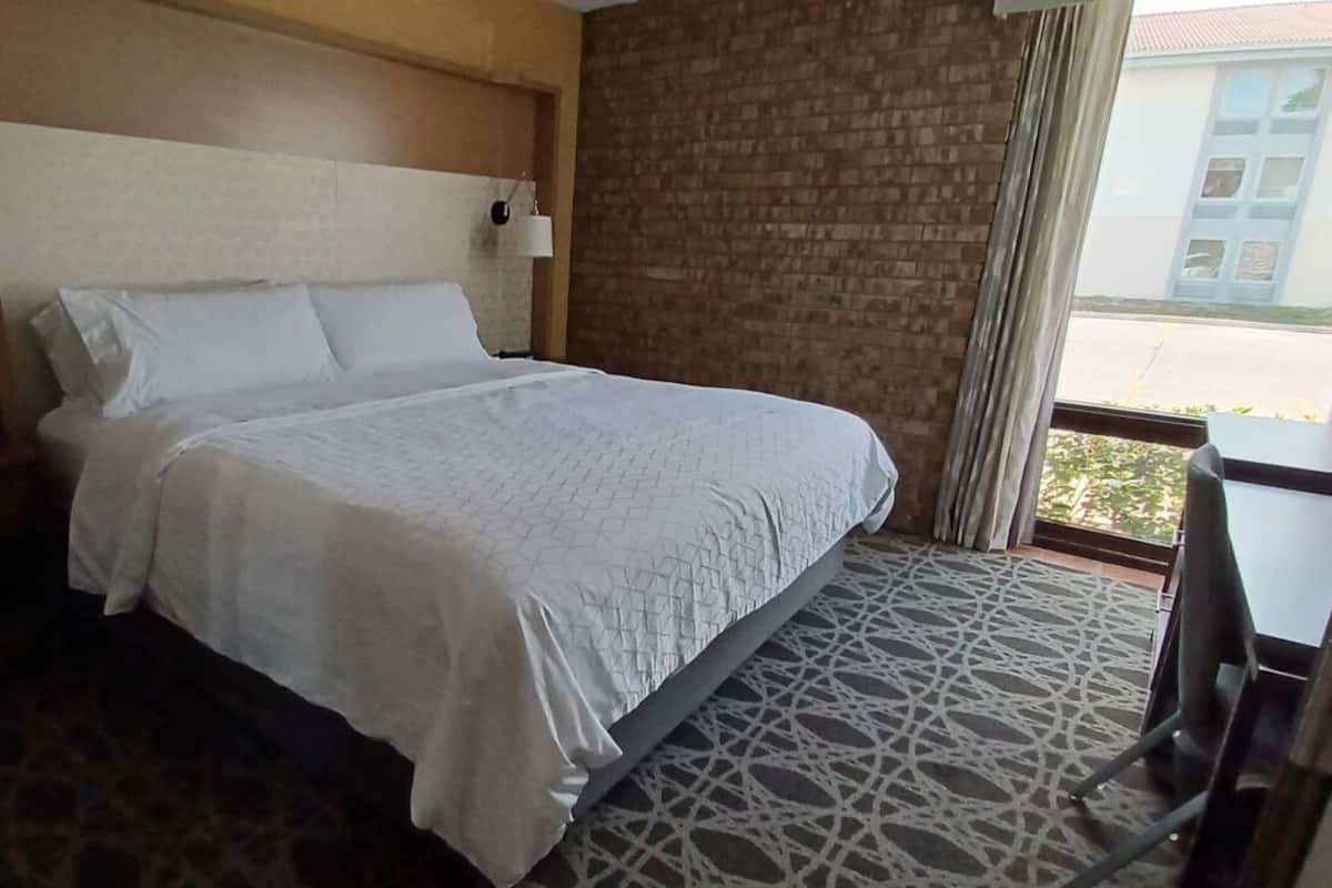 A hotel room with a large bed, a nightstand with a phone, a window with curtains, and a patterned carpet.