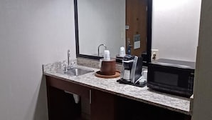 A bathroom with a sink, mirror, coffee maker, and microwave.