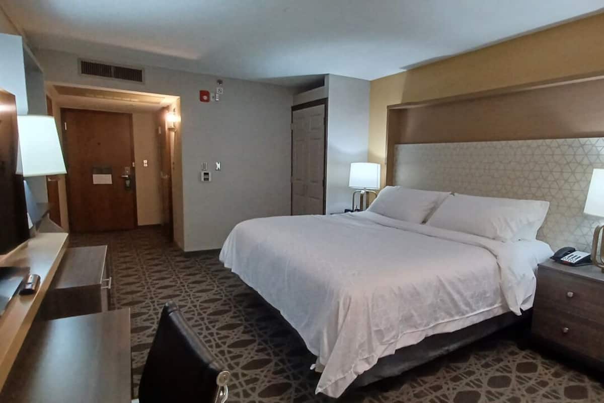 A hotel room with a bed, bedside tables, a desk, and a TV.