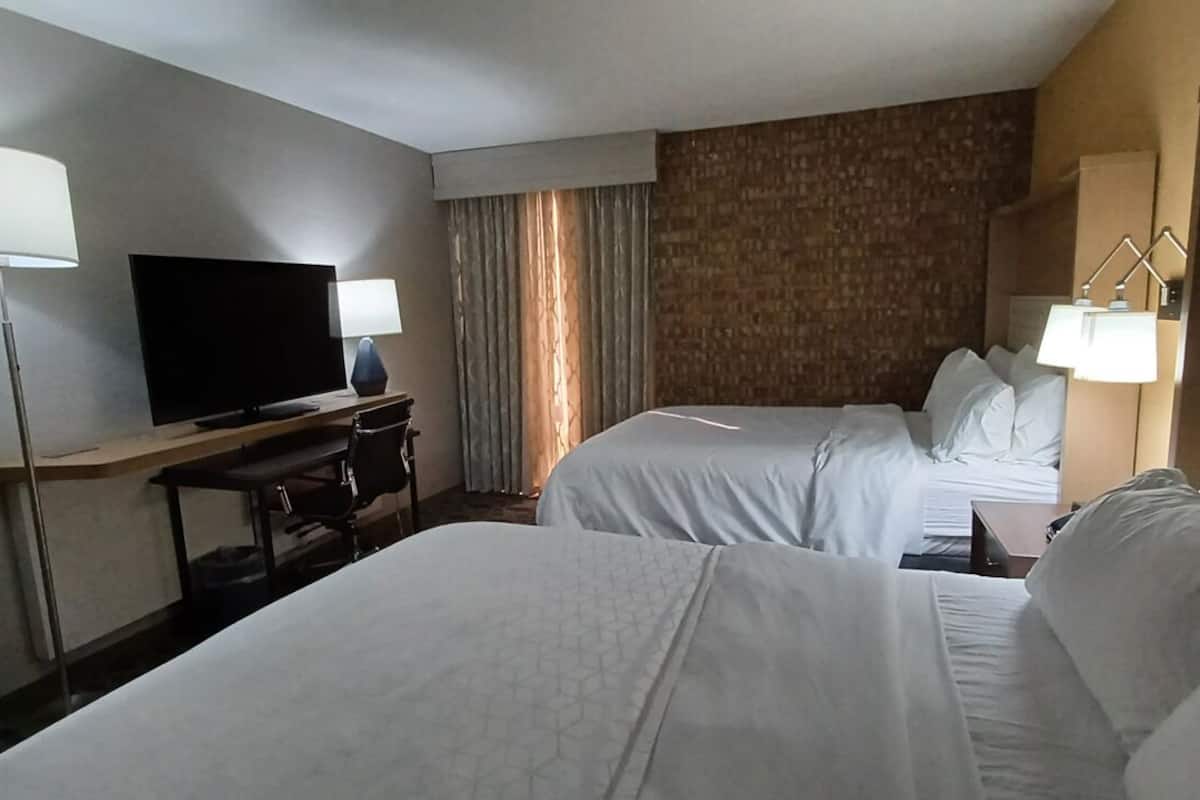 A hotel room with two beds, a TV, a desk, and a lamp.