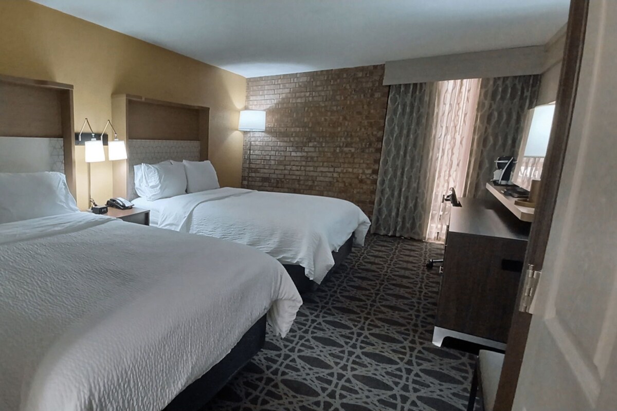 Una habitació d'hotel amb dos llits, una taula de treball i una paret de maó.
