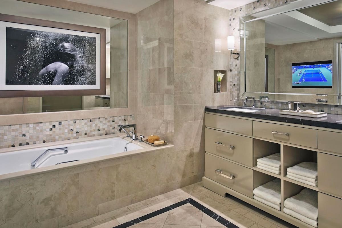 A modern bathroom with a large bathtub, a vanity with a mirror, and a television mounted on the wall.