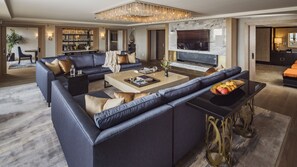 A modern living room with a sectional sofa, a coffee table, and a TV. There is a chandelier, a fireplace, and a bookshelf in the background. - L'Ermitage Beverly Hills (Beverly Hills)
