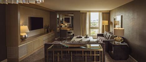 Una habitación de hotel moderna con televisión de pantalla plana, sofá, mesa de comedor y un ventanal con cortinas.