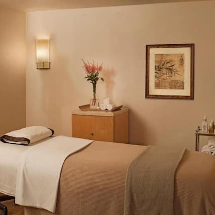 A spa room with two beds, a massage chair, wall-mounted lights, framed artwork, and a small table with toiletries.