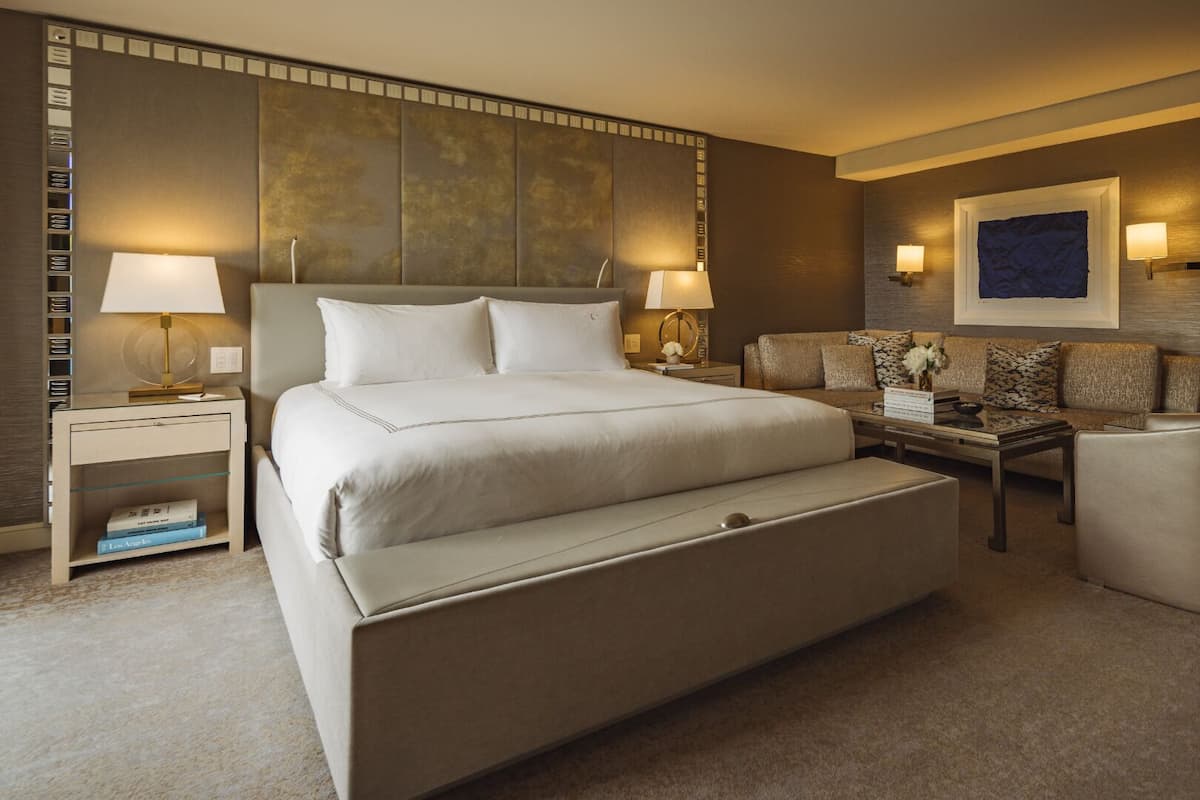 A hotel room with a large bed, a sofa, a coffee table, and two lamps.