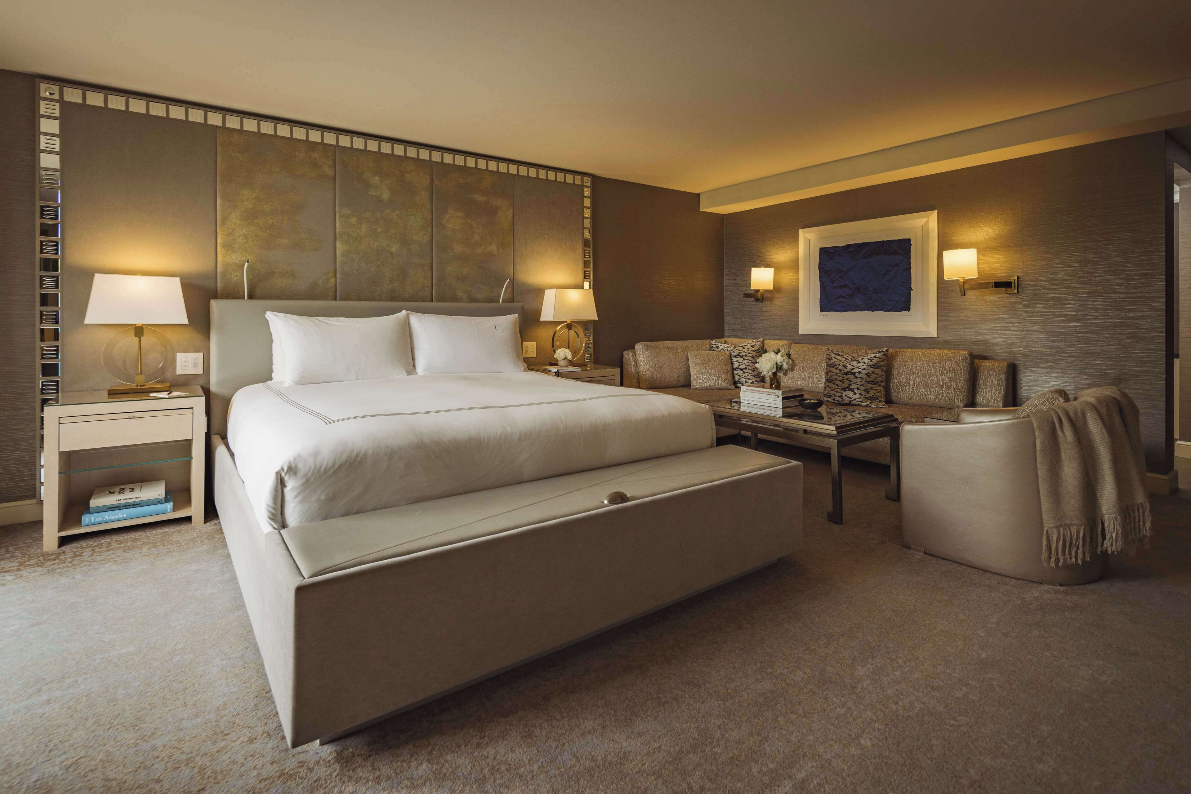 Ein Hotelzimmer mit einem großen Bett, zwei Nachttischen, einem Schlafsofa, einem Couchtisch und einem an der Wand montierten Fernseher.