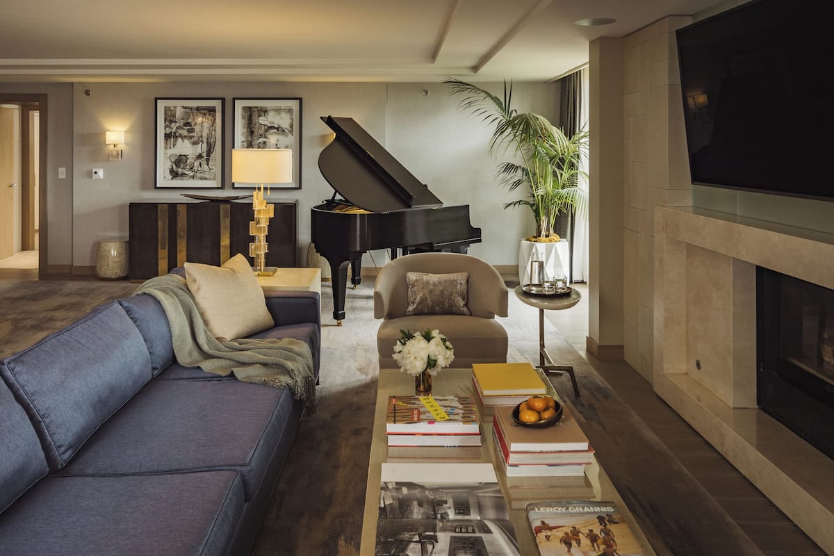 A living room with a grand piano, a sofa, a coffee table with books and a vase of flowers, and a television.