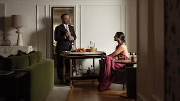 A room with a green sofa, a table with a tray of drinks, and a person standing by the door.