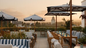 Eine Terrasse im Freien mit gestreiften, blauen und weißen Sofas, Holztischen und Sonnenschirmen.
