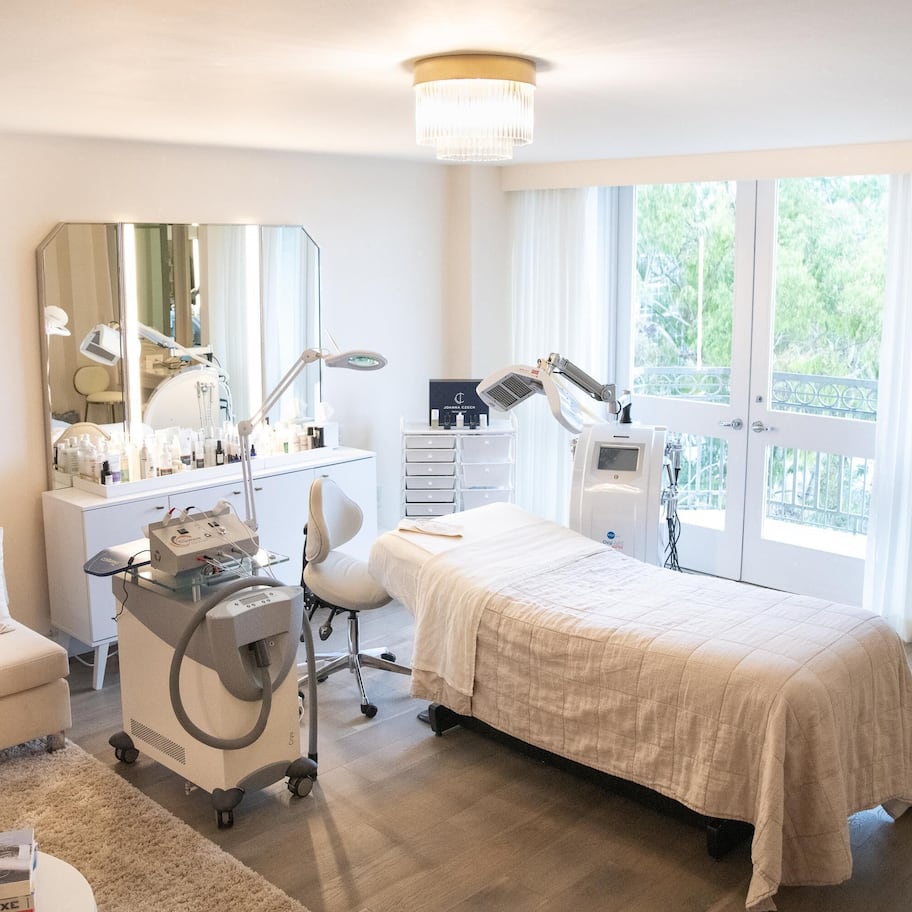 A bedroom with a bed, a desk, a chair, a vanity with a mirror, and a chandelier.