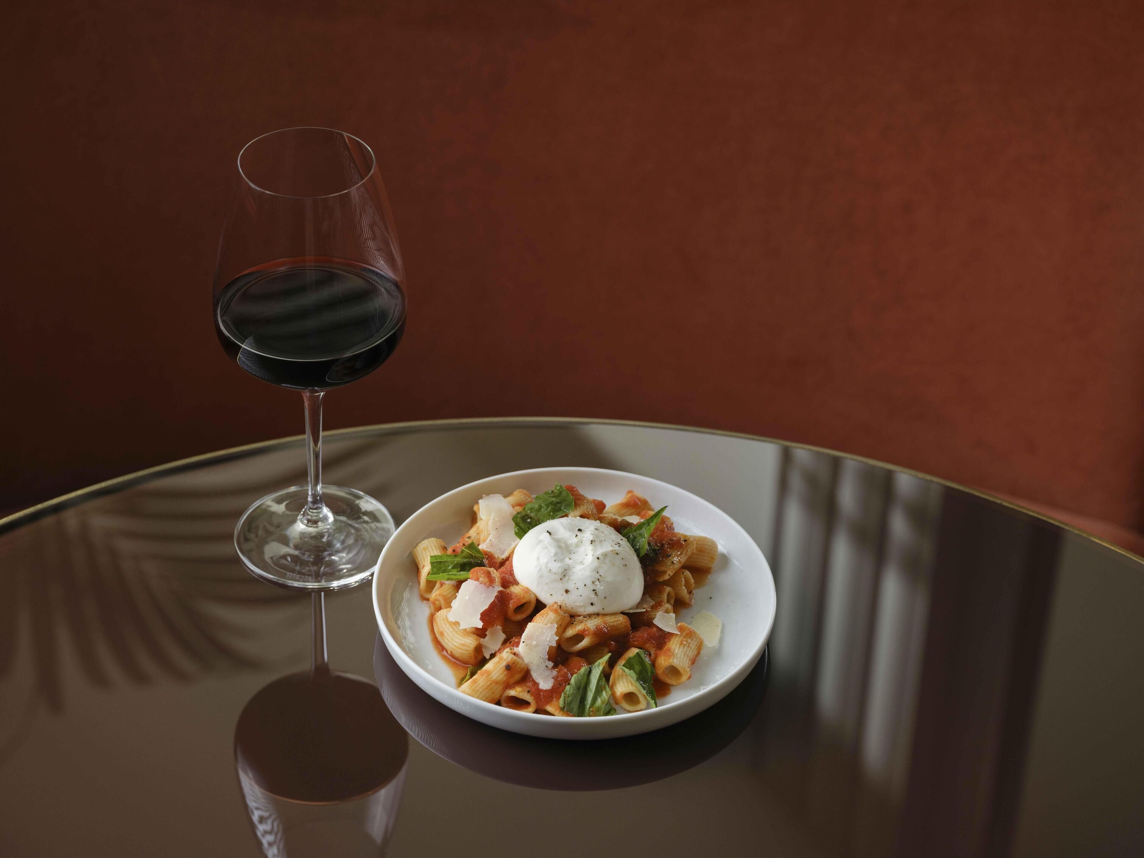 A plate of pasta with a poached egg and a glass of red wine on a reflective table.