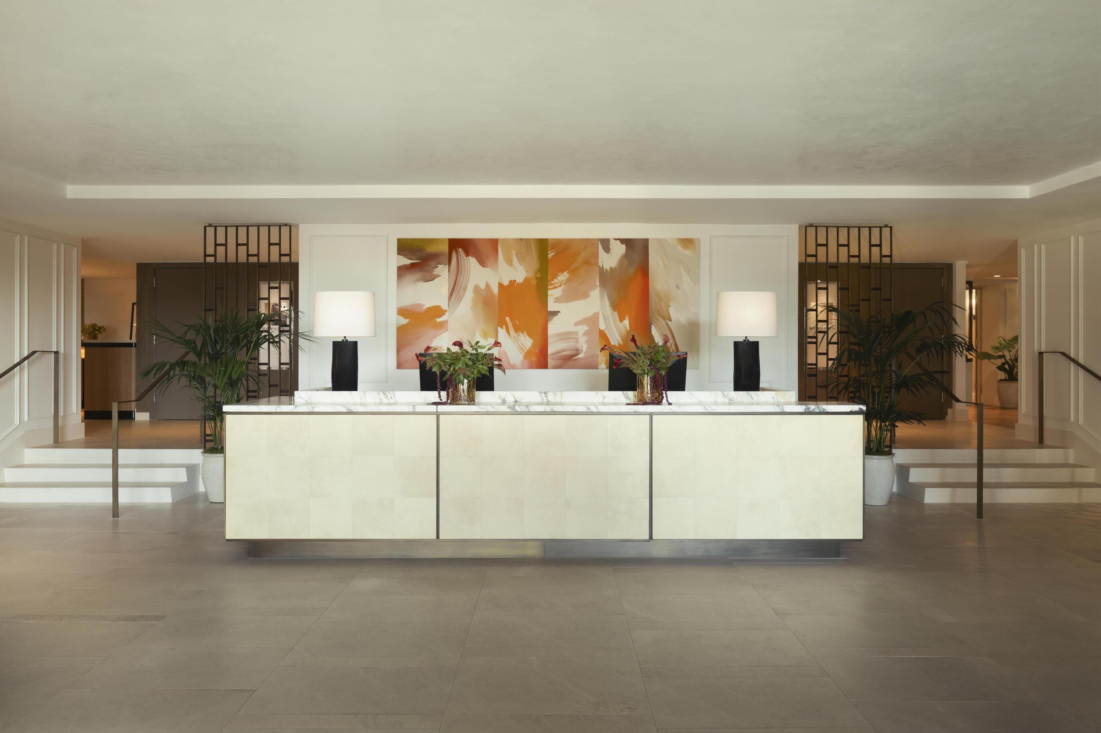 Um hall amplo com uma recepção central, duas grandes pinturas abstratas e plantas em vasos.
