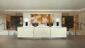 A spacious lobby with a central reception desk, two large abstract paintings, and potted plants.