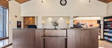 A reception area with a wooden reception desk, a clock on the wall, and a vending machine to the right.