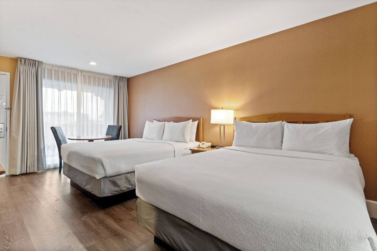 A hotel room with two beds, a desk, and a chair.