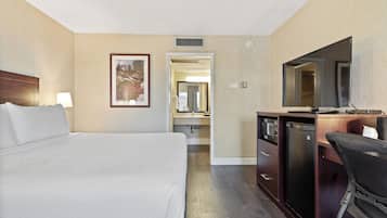 A hotel room with a bed, a desk with a television, a mirror, and a bathroom visible through an open door.