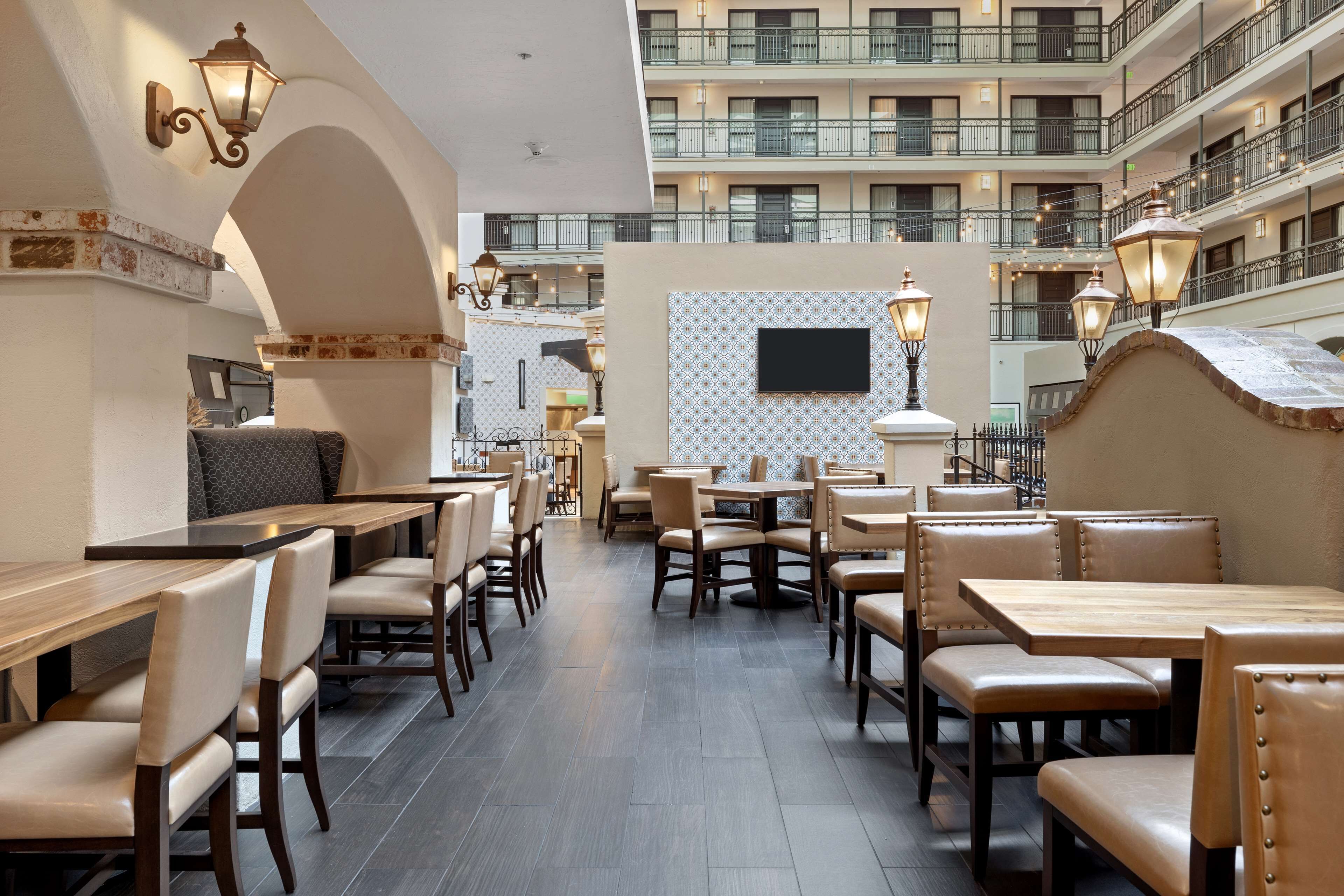 Ein Restaurant mit mehreren Tischen und Stühlen, einer Wand mit Muster und einem Balkon mit Geländern.