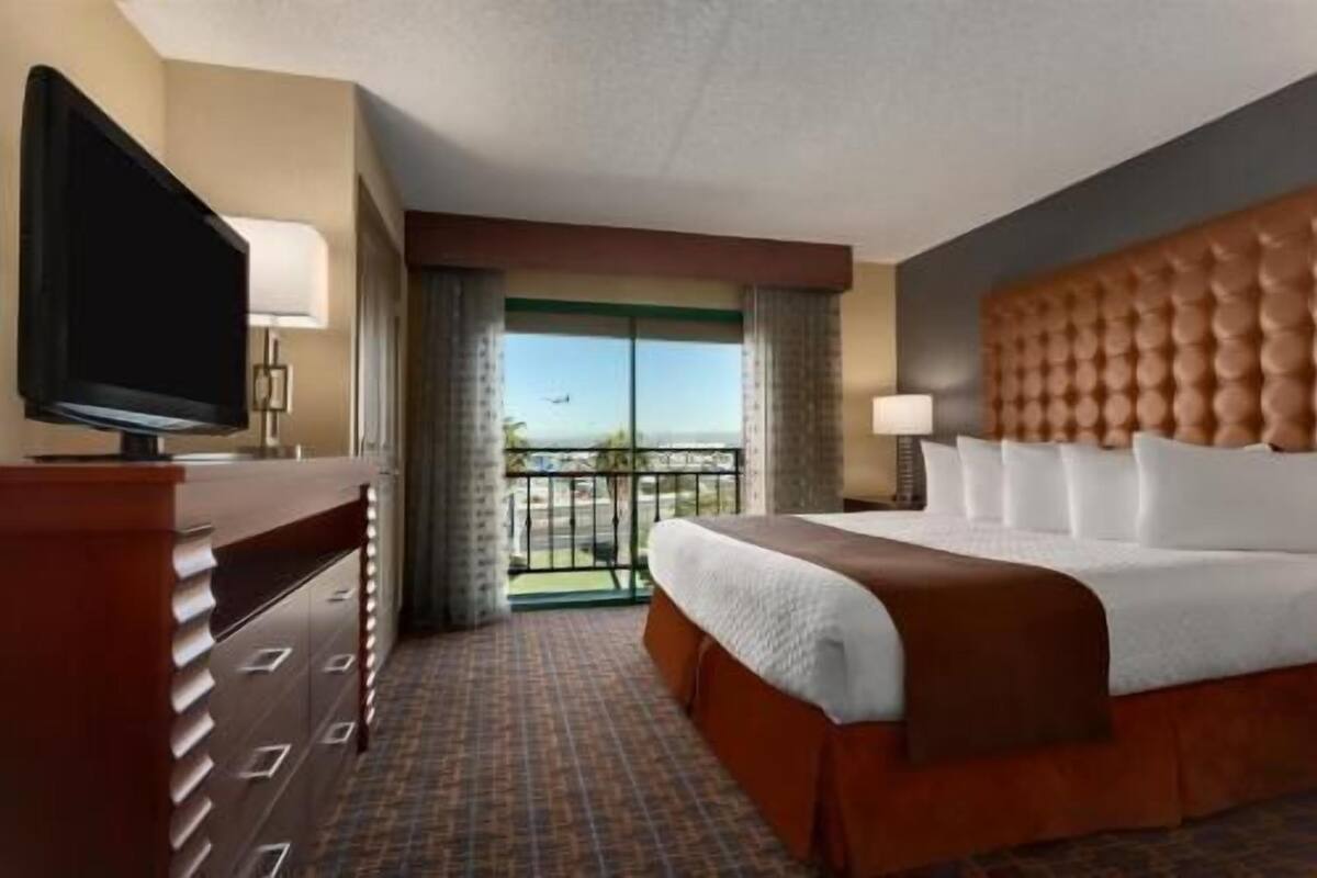 Habitación de hotel con cama, televisión, cómoda, lámpara y balcón con vistas.
