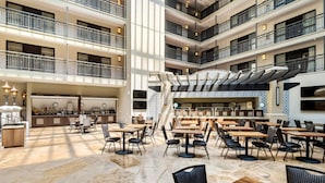 Un hall d’hôtel à plusieurs niveaux, doté d’un escalier central, d’un espace repas avec tables et chaises, et d’un coin cuisine.