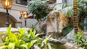 Un jardin intérieur luxuriant, agrémenté d’une cascade, de plantes en pot et de lampadaires de style ancien.