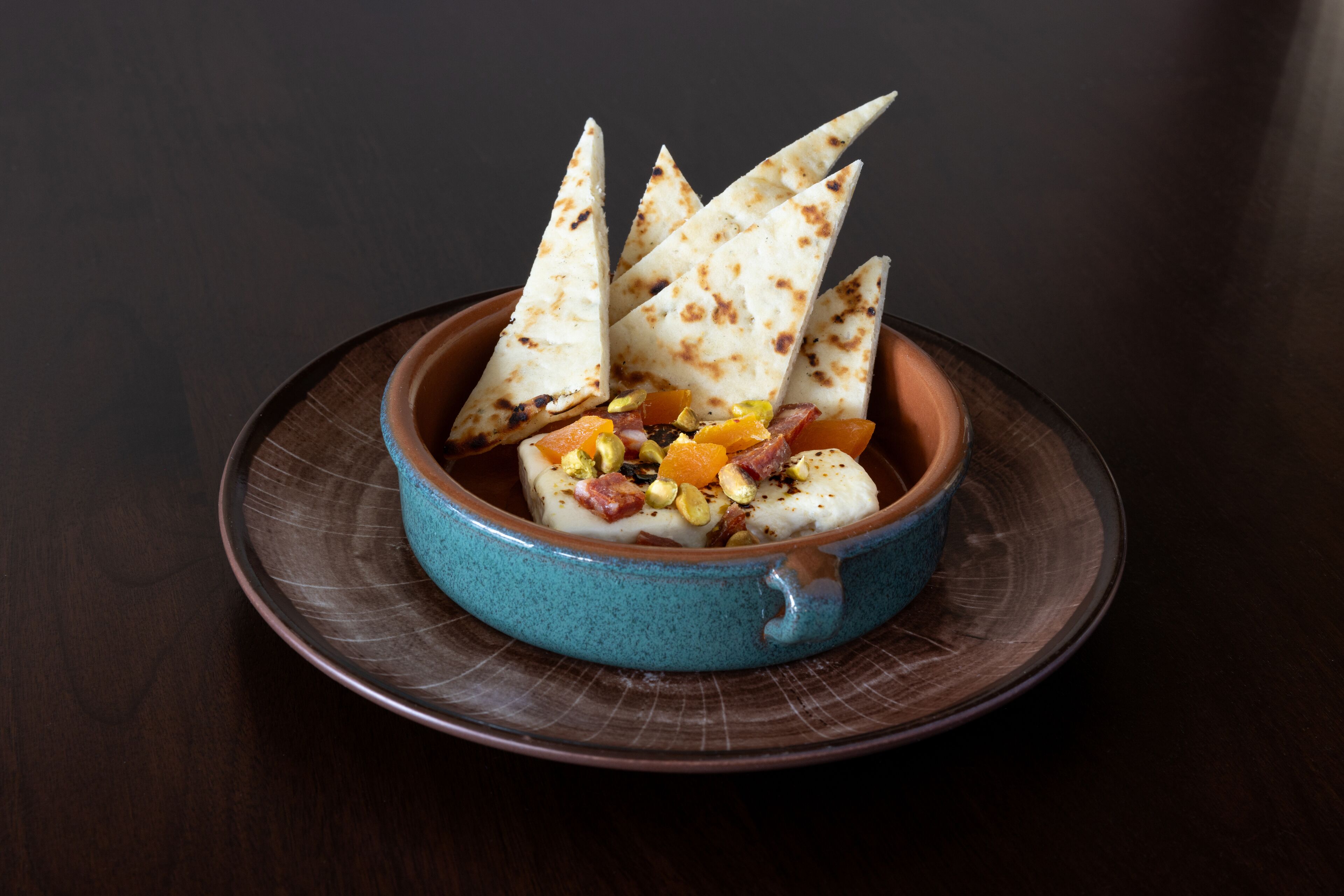 A dish with triangular pieces of flatbread, orange segments, and nuts in a blue bowl on a dark plate.