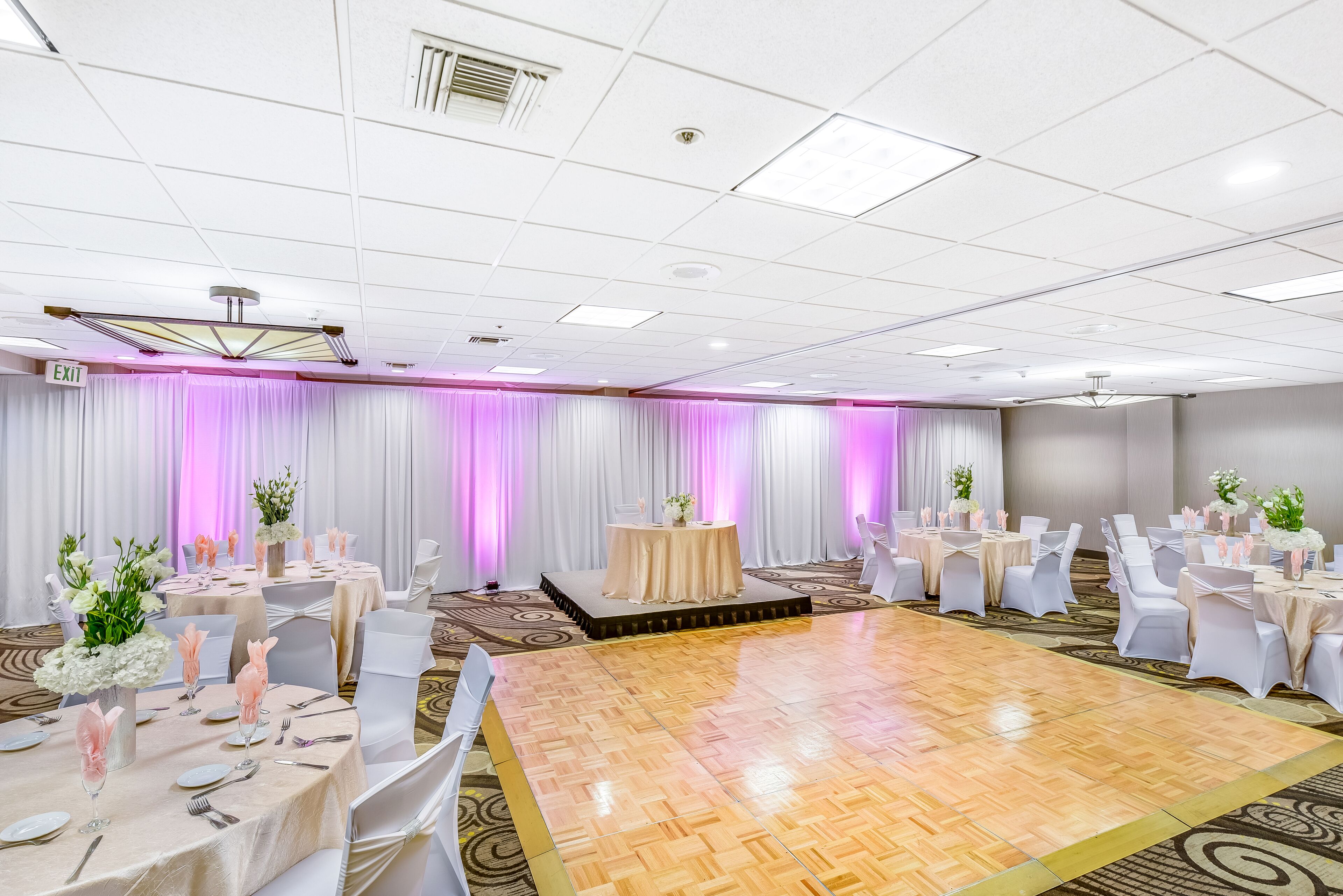 A banquet hall with round tables, white chairs, and a dance floor.