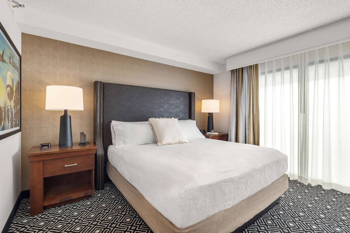 Habitación de hotel con una cama grande, dos mesitas de noche con lámparas, un cabecero y un piso con diseño.