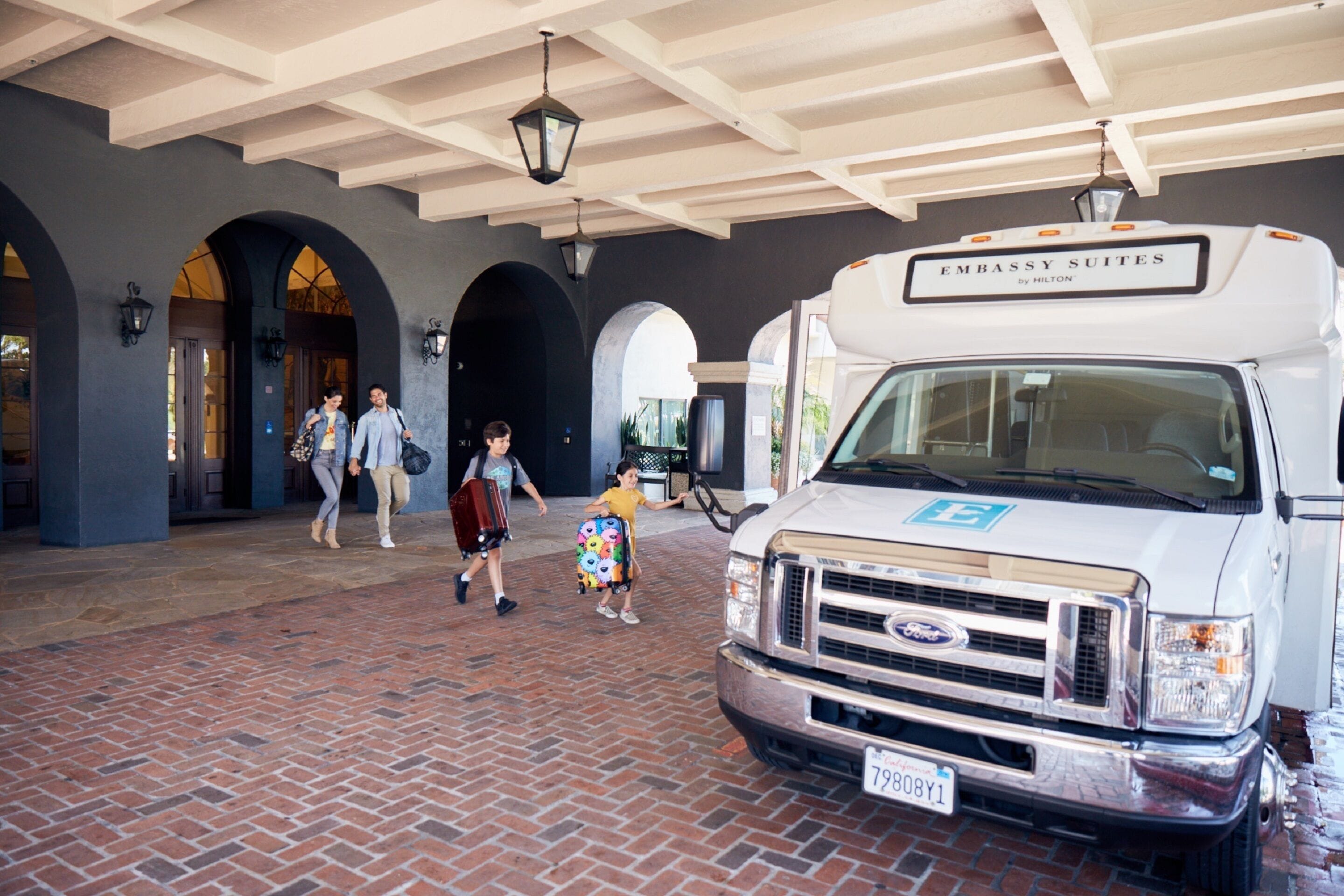 A white RV with "Embassy Suites" branding parked under a covered area with brick flooring and arched doorways.
