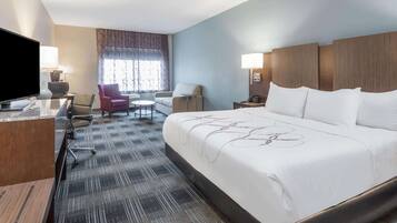 A hotel room with a large bed, a desk with a computer, a chair, a small table, and a TV.