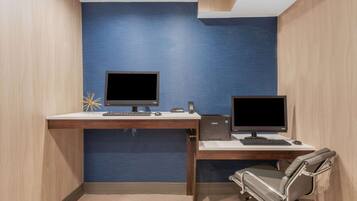 Een moderne kantoorruimte met twee bureaus, elk met een computerscherm, toetsenbord en muis. Er staat een stoel bij het rechter bureau. De ruimte heeft houten wanden en een blauwe accentmuur.