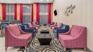 Vestíbulo de hotel con zonas de estar, un televisor en la pared y cortinas estampadas.