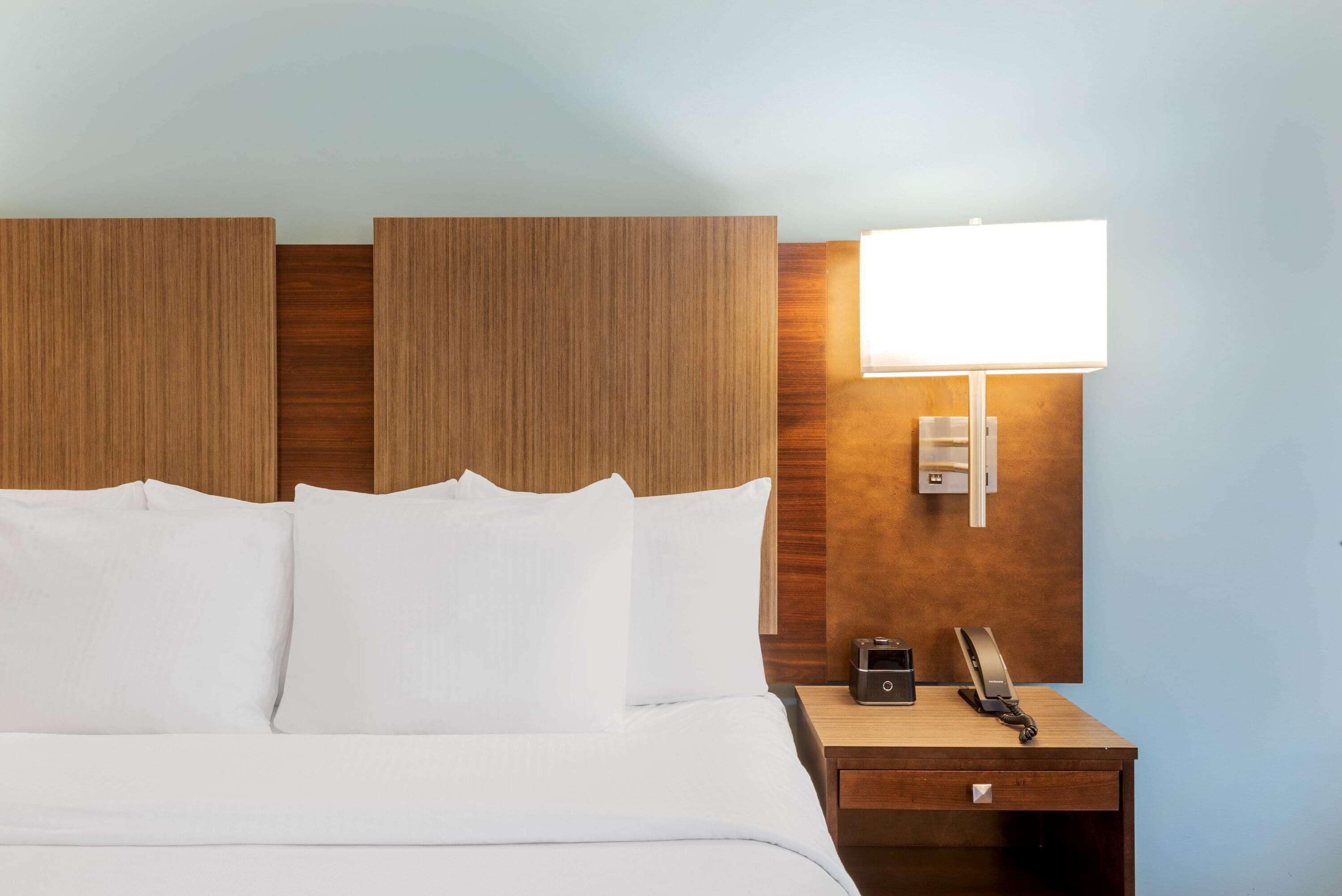 Una habitación de hotel con una cama, una mesita de noche con lámpara y un teléfono.