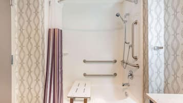 Een moderne badkamer met een douche, handgrepen, een klein krukje en een bad.